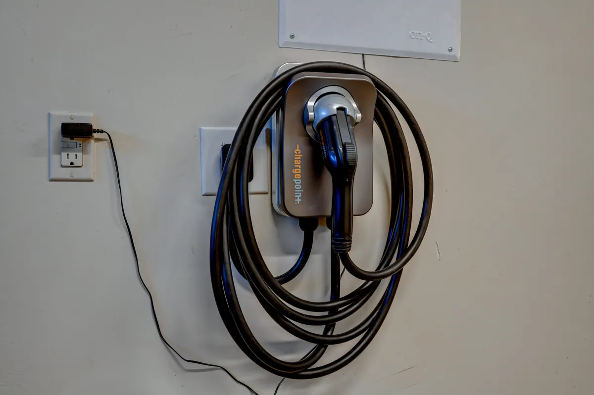 A clean, organized garage featuring a prominently placed electric vehicle charging station with its charging cable. The space is tidy, modern, and hints at practical amenities available for guests.