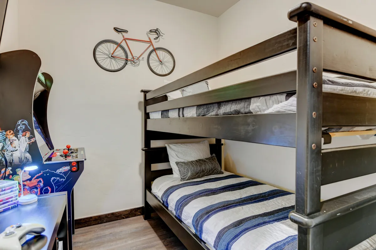 A playful bunk room furnished with a twin bunk bed, decorative touches like a bicycle and an arcade game, and a cozy, inviting layout. The room feels welcoming and fun, ideal for children or groups of friends.