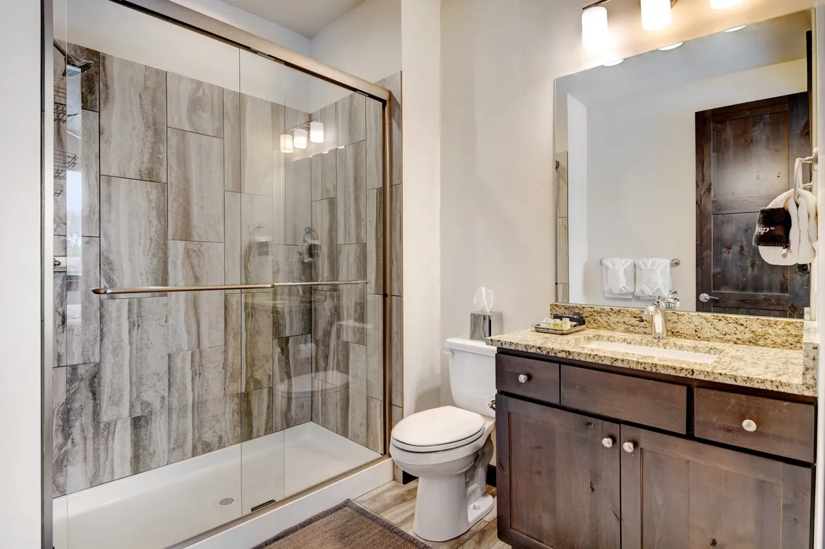 A modern, spa-inspired bathroom with a glass shower enclosure, granite countertop, dark wood cabinetry, and a mirrored vanity. The space looks fresh and tranquil, perfect for unwinding after a day of adventure.
