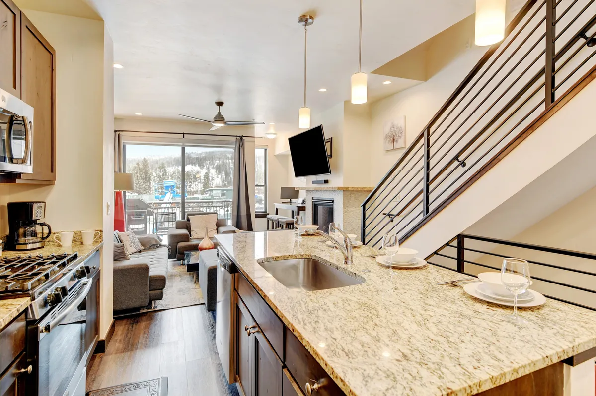 A stylish open-concept space unites the kitchen island and adjacent dining area, flowing into a living area with comfortable seating and large windows. The design emphasizes seamless movement and group gatherings, perfect for celebrations or relaxed meals.