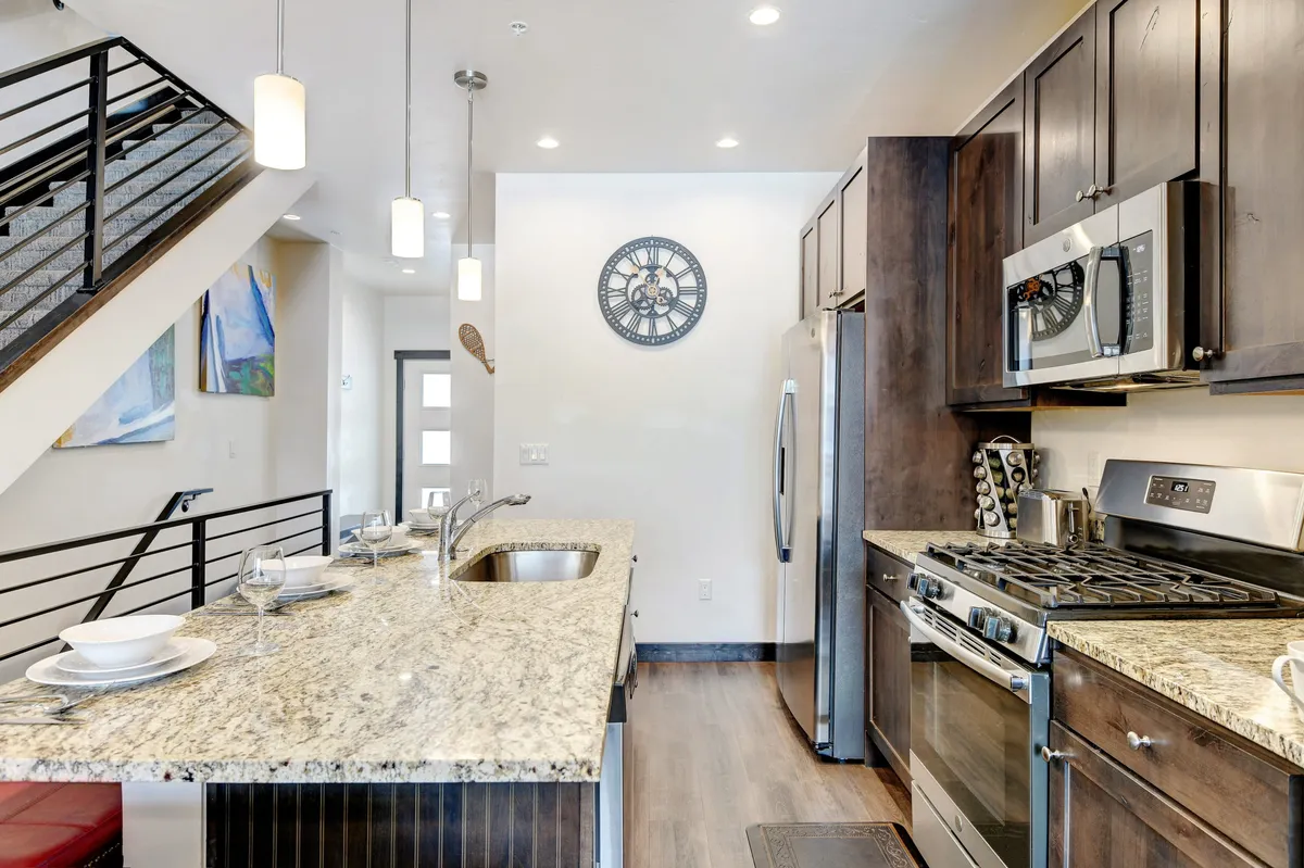 This image showcases a spacious, modern kitchen with granite countertops, stainless steel appliances, elegant pendant lighting, and a central kitchen island. The layout invites meal preparation and social gatherings, emphasizing high-end finishes and functionality.