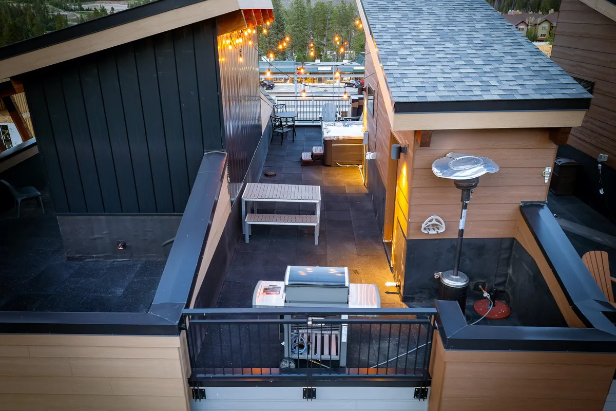 This image features a stylish rooftop seating area illuminated by custom string lights. Comfortable seating and a barbecue grill are arranged to encourage group dining and relaxed social gatherings, with heaters ensuring comfort even in cooler weather.