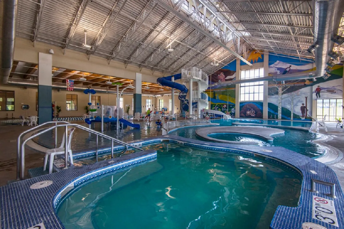 A vibrant indoor recreation center filled with swimming pools, colorful murals, twisting water slides, and children engaged in play and family bonding activities.