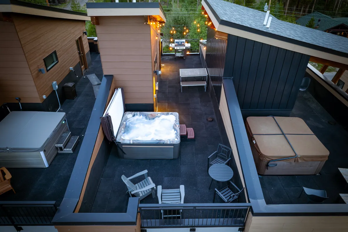 A festive outdoor rooftop space with a hot tub, a comfortable seating area, string lights overhead, and a barbecue grill at the ready. The area is set up for both relaxation and socializing, with an inviting atmosphere perfect for gatherings or quiet evenings under the stars.
